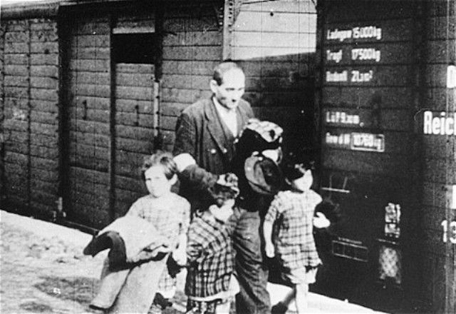 A Jewish man walks with three young children alongside a deportation train in the Warsaw ghetto